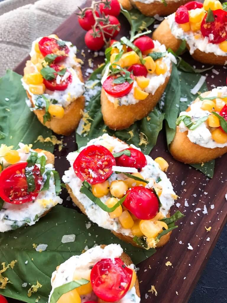 Fresh cherry tomatoes, basil, and corn are mixed with lemon. Ricotta and Parmesan cheese are mixed with lemon and herbs then layered on toasted bread slices. Tomato Corn Basil Crostini with Herbed Ricotta Cheese are vegetarian and perfect party and summer entertaining food. #fingerfood #summerappetizer #crostini