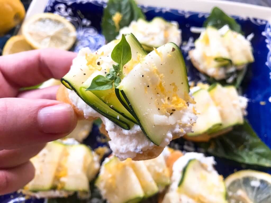 A hand holding a slice of toast with cheese and squash on it