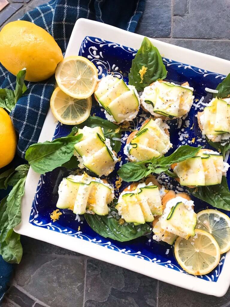 A plate of Zucchini Lemon Ricotta Crostini surrounded by basil