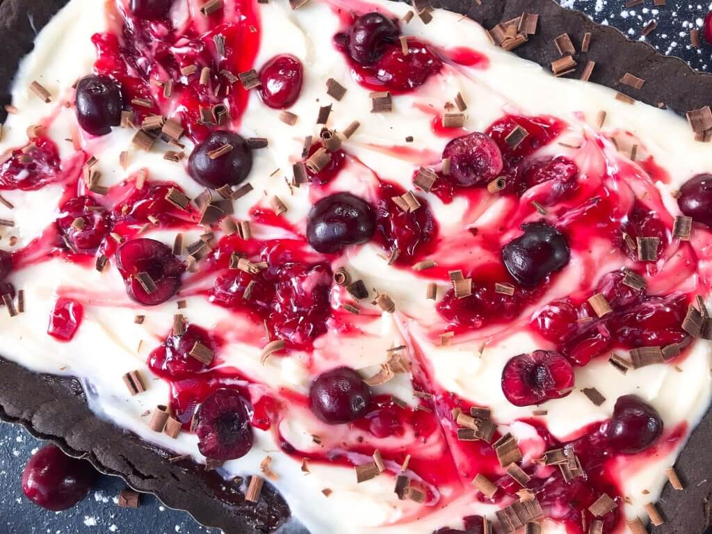 A quick and simple Black Forest Tart dessert recipe ready in 30 minutes. Chocolate, cherries, and cream are combined with a cocoa crust, cream cheese filling, and cherry pie swirl. #blackforestdesserts #tartrecipe #cherrydessert