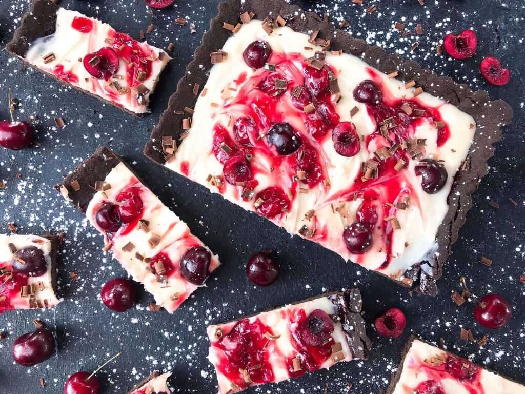 A quick and simple Black Forest Tart dessert recipe ready in 30 minutes. Chocolate, cherries, and cream are combined with a cocoa crust, cream cheese filling, and cherry pie swirl. #blackforestdesserts #tartrecipe #cherrydessert