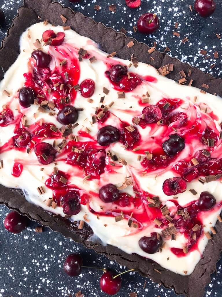 A quick and simple Black Forest Tart dessert recipe ready in 30 minutes. Chocolate, cherries, and cream are combined with a cocoa crust, cream cheese filling, and cherry pie swirl. #blackforestdesserts #tartrecipe #cherrydessert