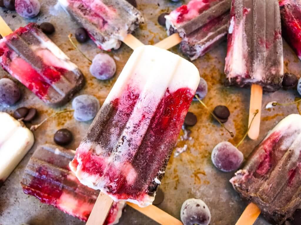 Black Forest Yogurt Popsicles are a simple and quick frozen dessert treat perfect for summer. Greek yogurt, cocoa chocolate yogurt, and cherry pie filling are layered for a healthy dessert. Vegetarian. #blackforest #cherrychocolate #popsicles