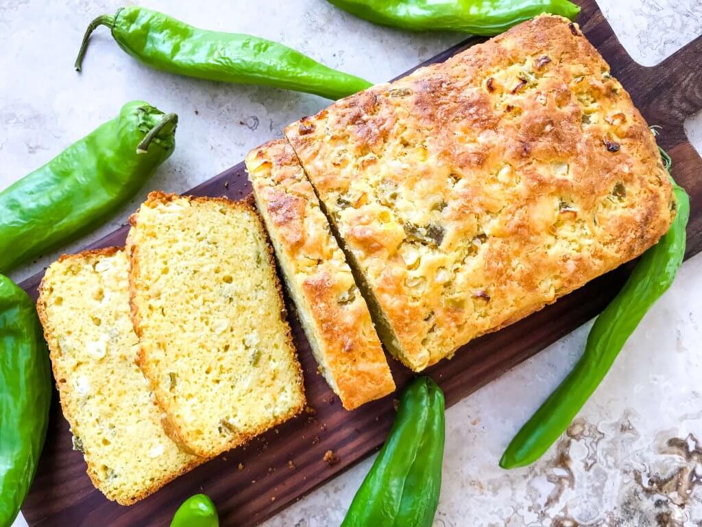 To view of a loaf and slices of Hatch Green Chile Cheddar Cornbread surrounded by chiles