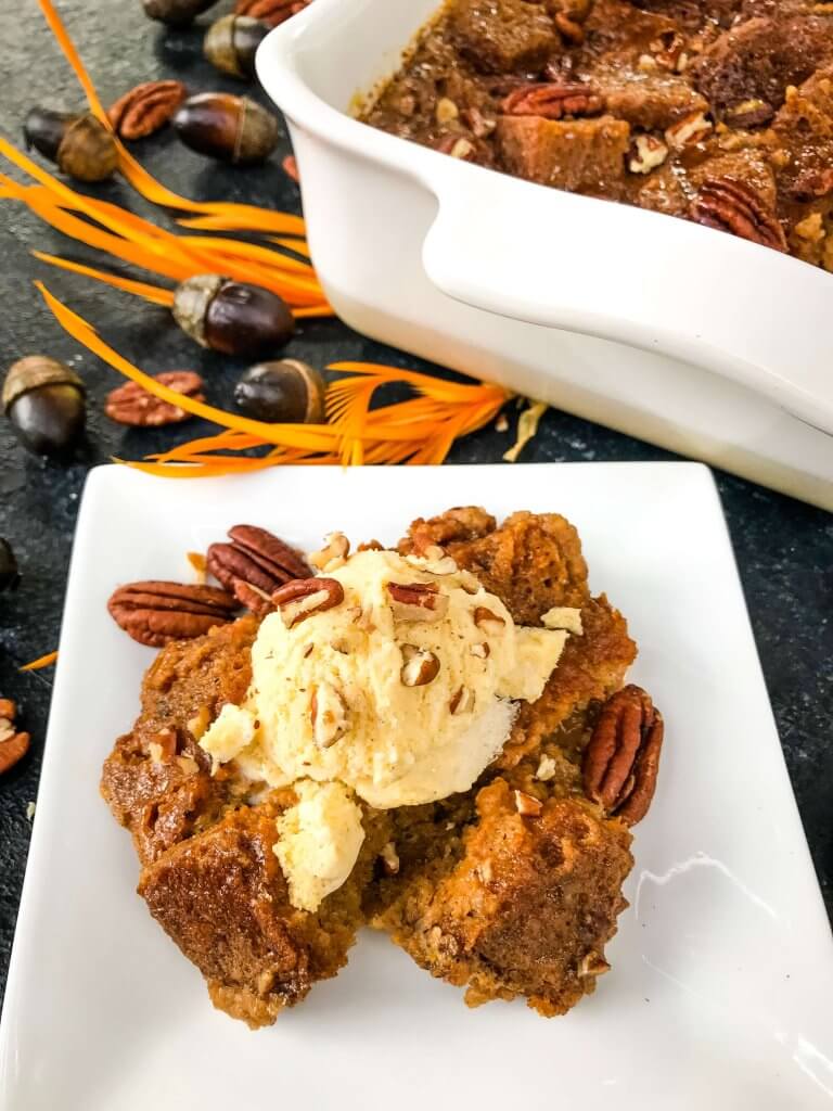 A portion of Pumpkin Bread Pudding on a white plate next to the casserole dish