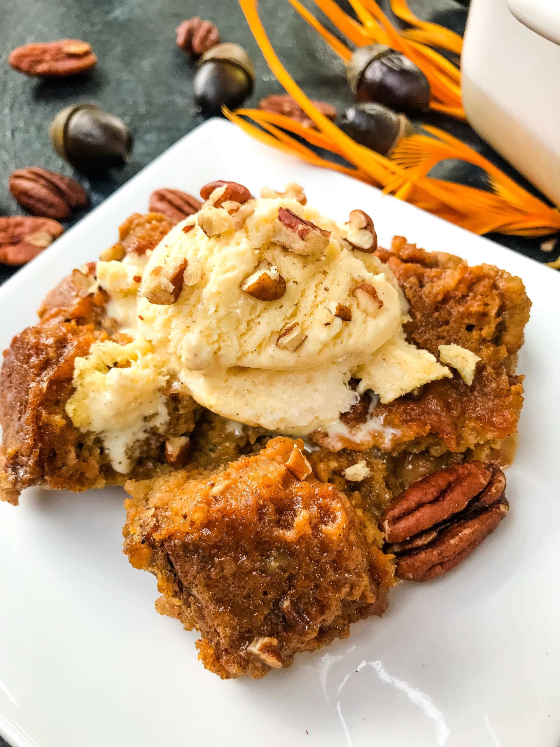 A postion of Pumpkin Bread Pudding on a white plate with vanilla ice cream on top