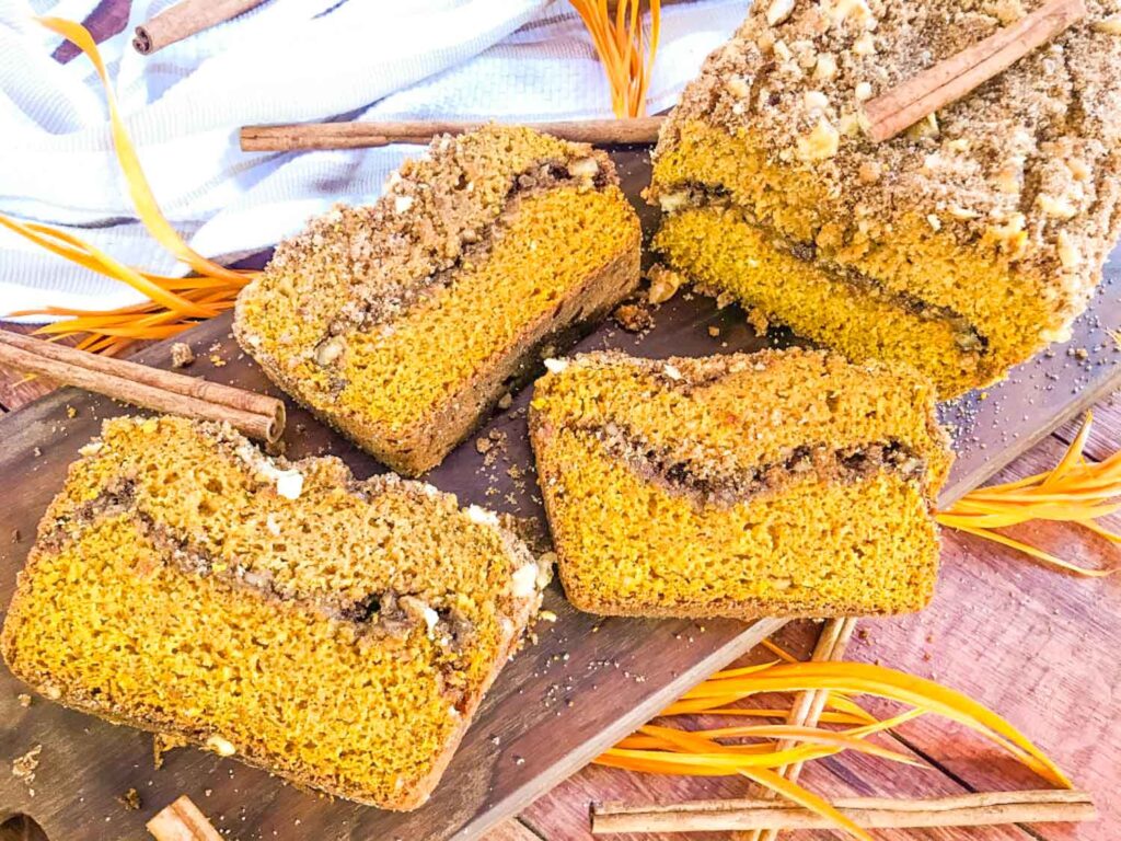 Slices of Cinnamon Streusel Pumpkin Bread laying next to half a loaf on a board