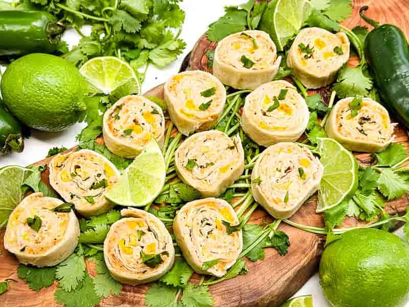 Mexican Street Corn Pinwheels on a wood board on a counter with fresh cilantro everywhere.