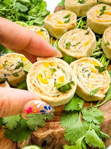 A hand holding a Mexican Street Corn Pinwheel roll up after picking up from a board of them.