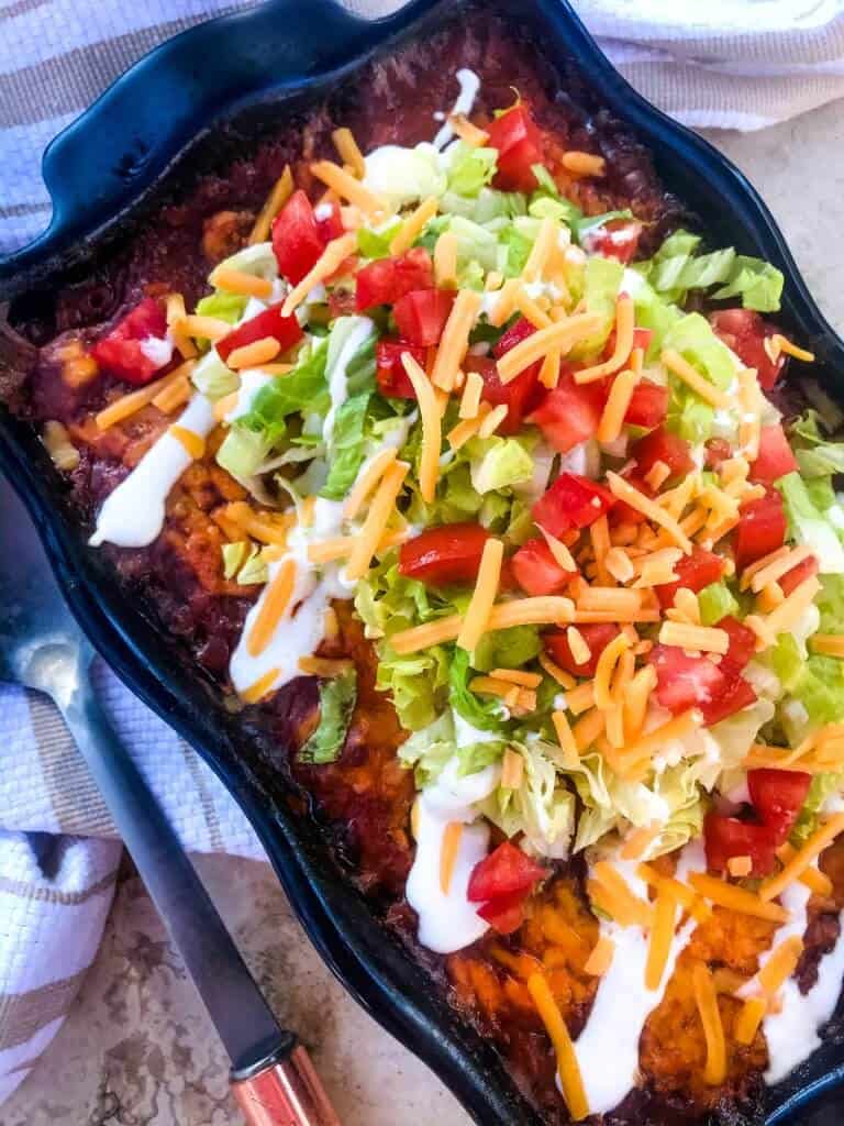 Beef Taco Tater Tot Casserole is a cheesy beef casserole seasoned like tacos with cheddar cheese and potato tater tots. Topped with all the taco toppings. An easy dinner idea for busy nights for the family. #beefcasserole #beeftacos #hamburgercasserole