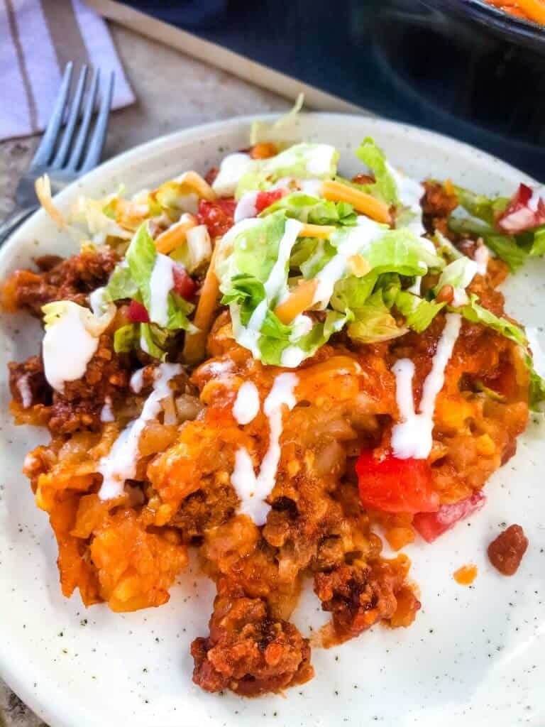 Beef Taco Tater Tot Casserole is a cheesy beef casserole seasoned like tacos with cheddar cheese and potato tater tots. Topped with all the taco toppings. An easy dinner idea for busy nights for the family. #beefcasserole #beeftacos #hamburgercasserole