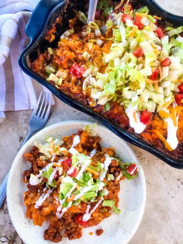 Beef Taco Tater Tot Casserole is a cheesy beef casserole seasoned like tacos with cheddar cheese and potato tater tots. Topped with all the taco toppings. An easy dinner idea for busy nights for the family. #beefcasserole #beeftacos #hamburgercasserole