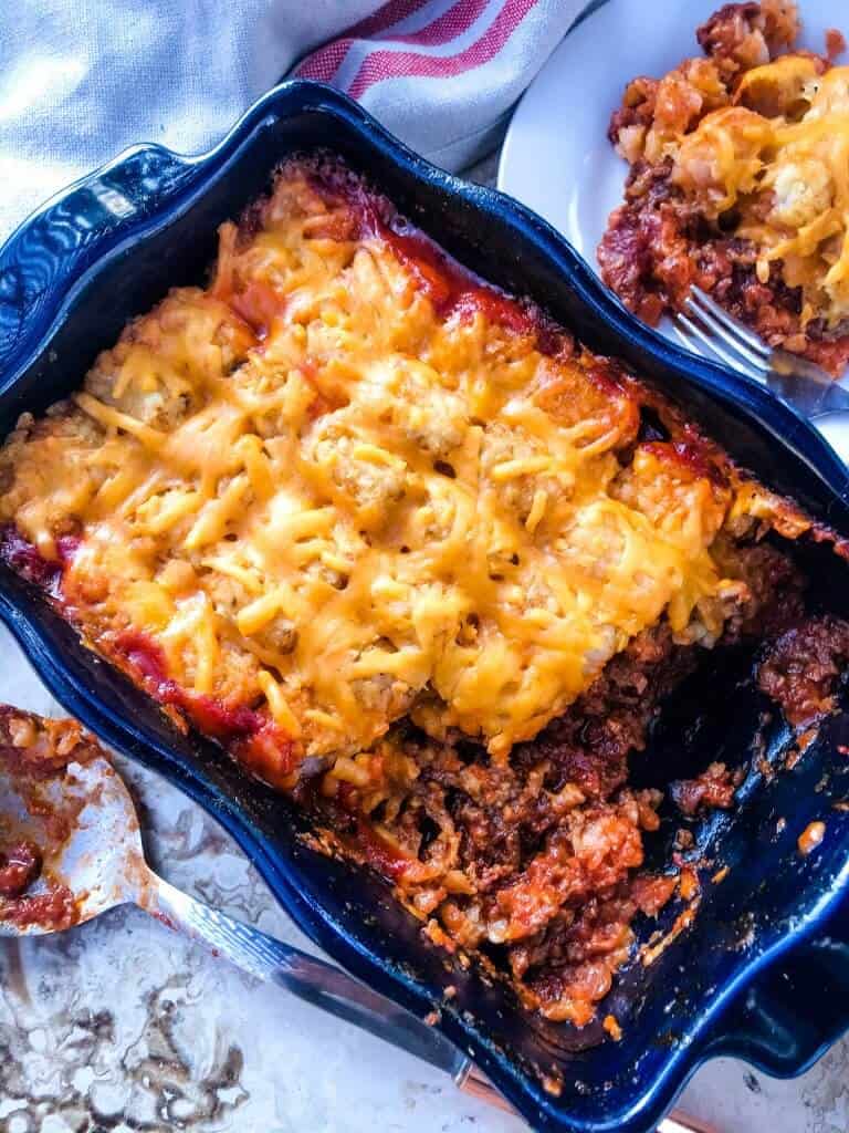 A blue dish filled with Beef Sloppy Joe Tater Tot Casserole with some missing