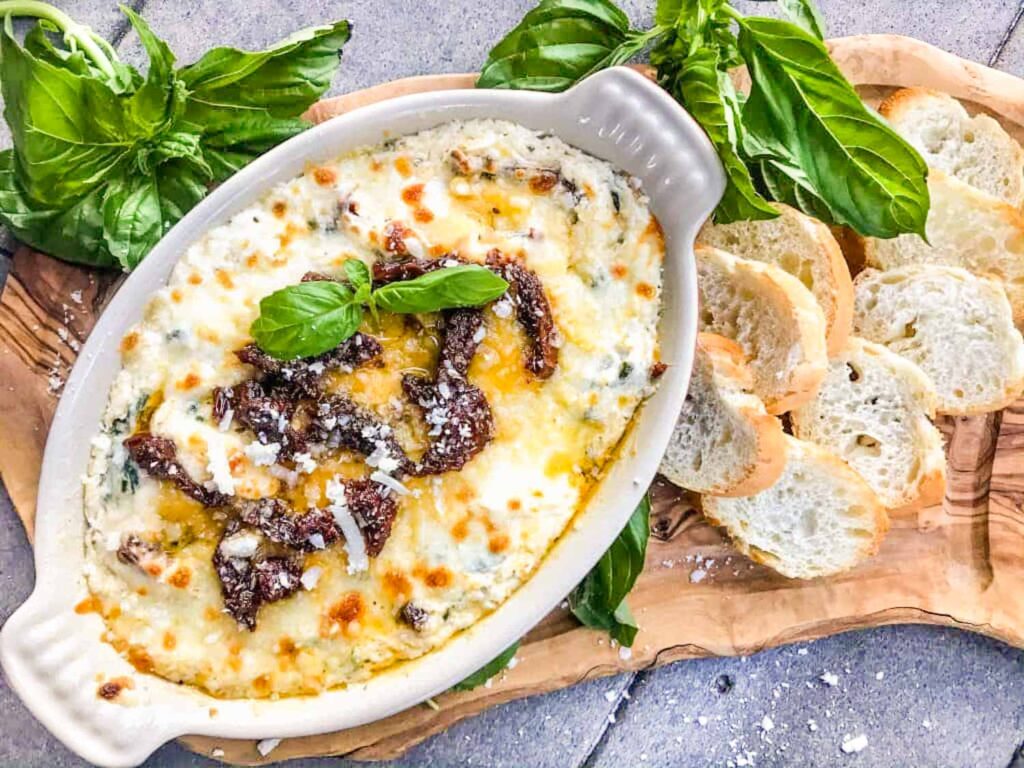 A dish of Tuscan Cheese Dip on a board with crostini and basil