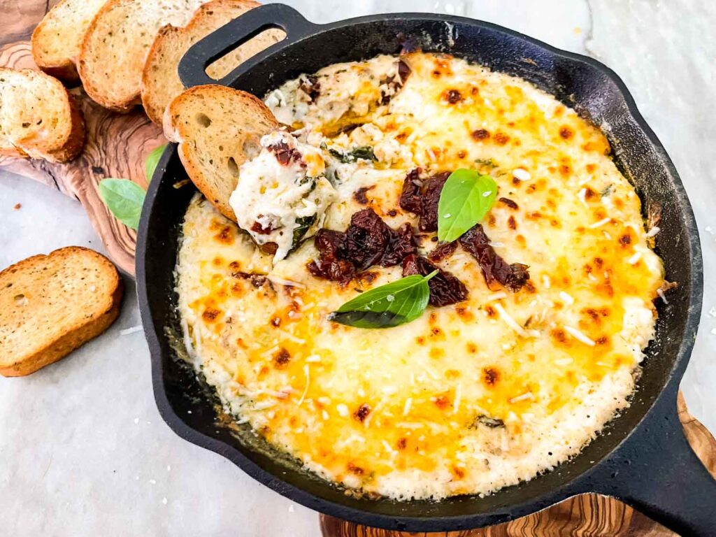 Tuscan Cheese Dip in a skillet with a piece of bread in it