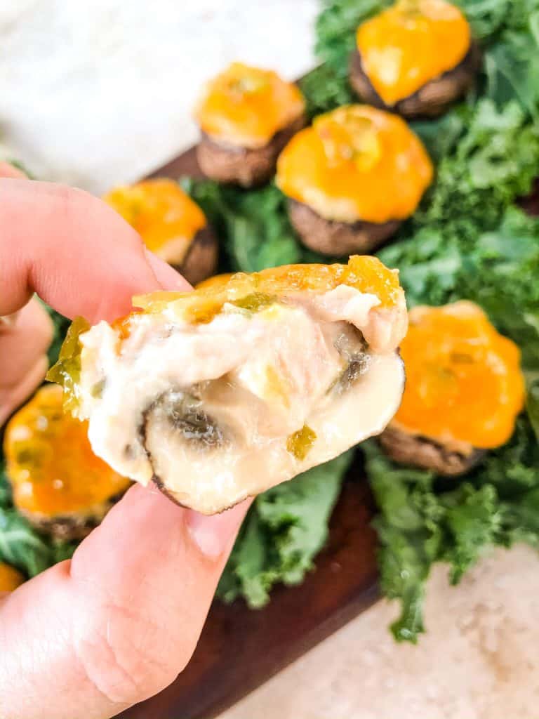 A hand holding a mushroom with tuna and cheddar that has been cut in half