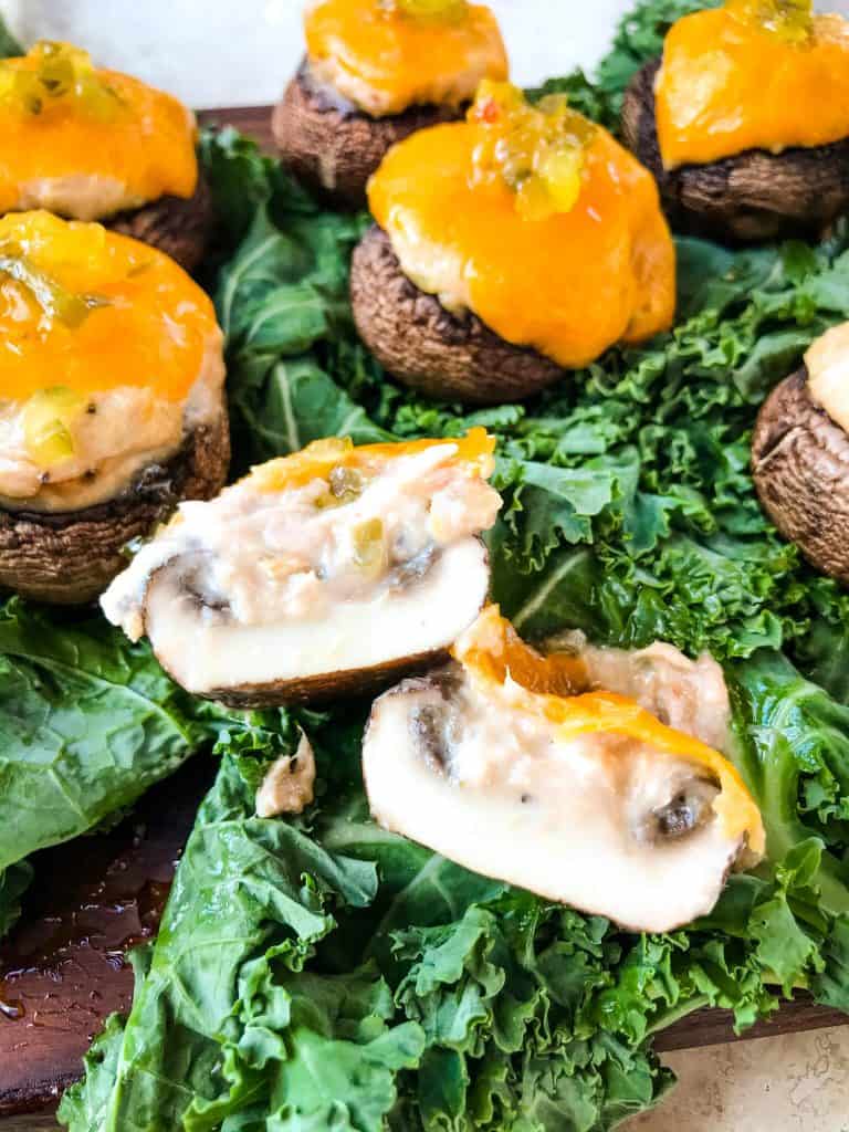 A Tuna Melt Stuffed Mushroom sliced open on lettuce with more mushrooms in the background