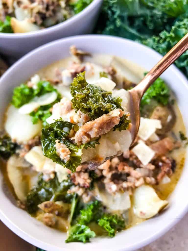 A spoon with a big scoop of Copycat Olive Garden Zuppa Toscana above the bowl