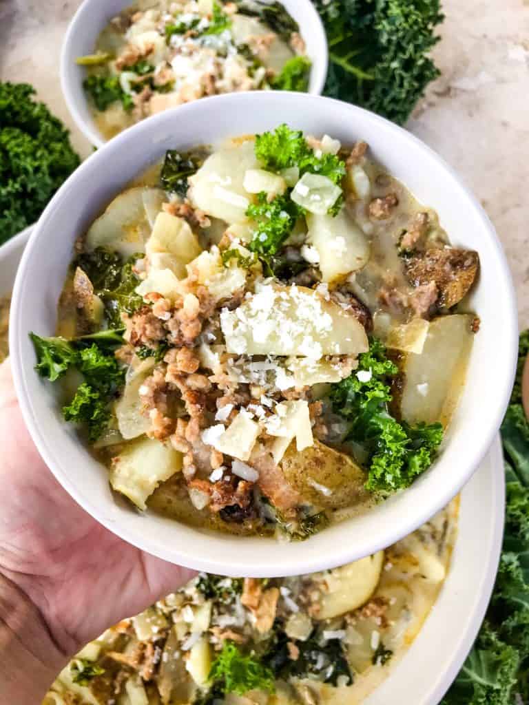 A hand holding a bowl of Copycat Olive Garden Zuppa Toscana