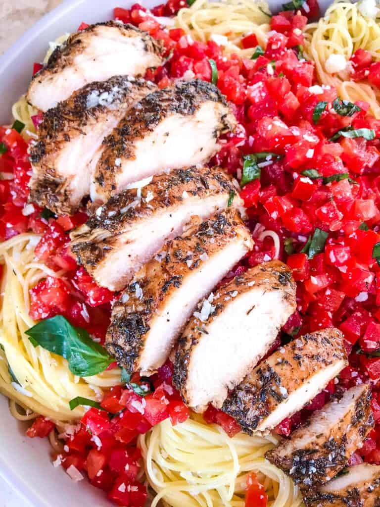 A close up of sliced balsamic chicken on top of chopped tomatoes and pasta