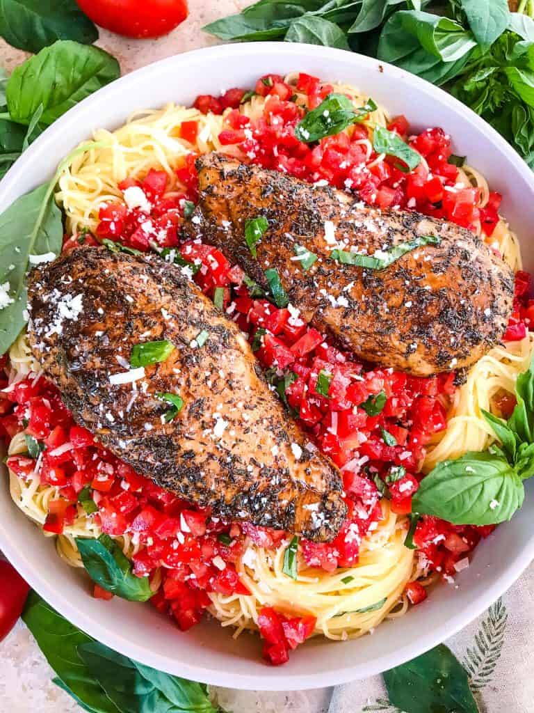 A bowl of Balsamic Chicken Bruschetta Pasta surrounded by basil