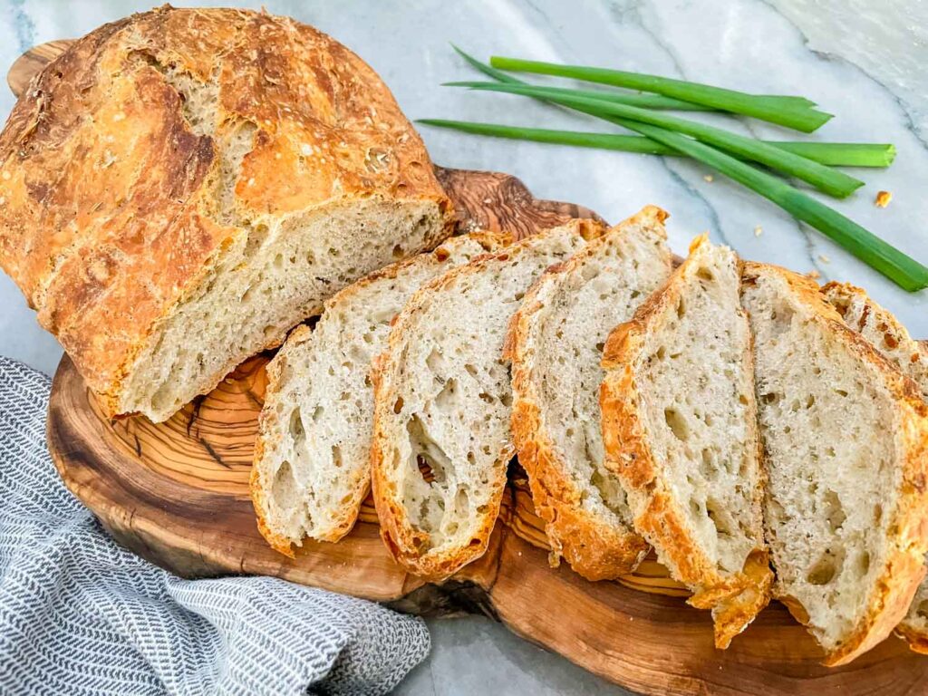 No Knead Rustic Rosemary Bread loaf half sliced on a wood board