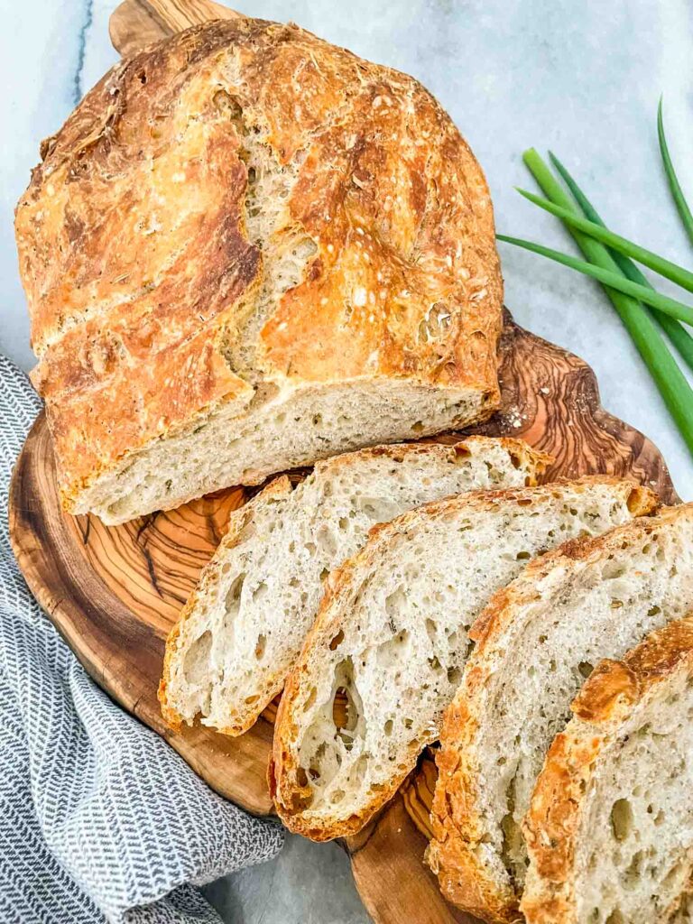 A No Knead Rustic Rosemary Bread loaf half sliced on a wood board