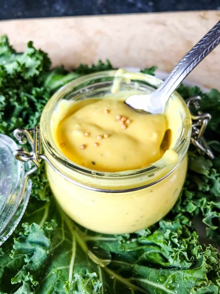 A spoon in a small clear jar of Homemade Creamy Honey Mustard Sauce