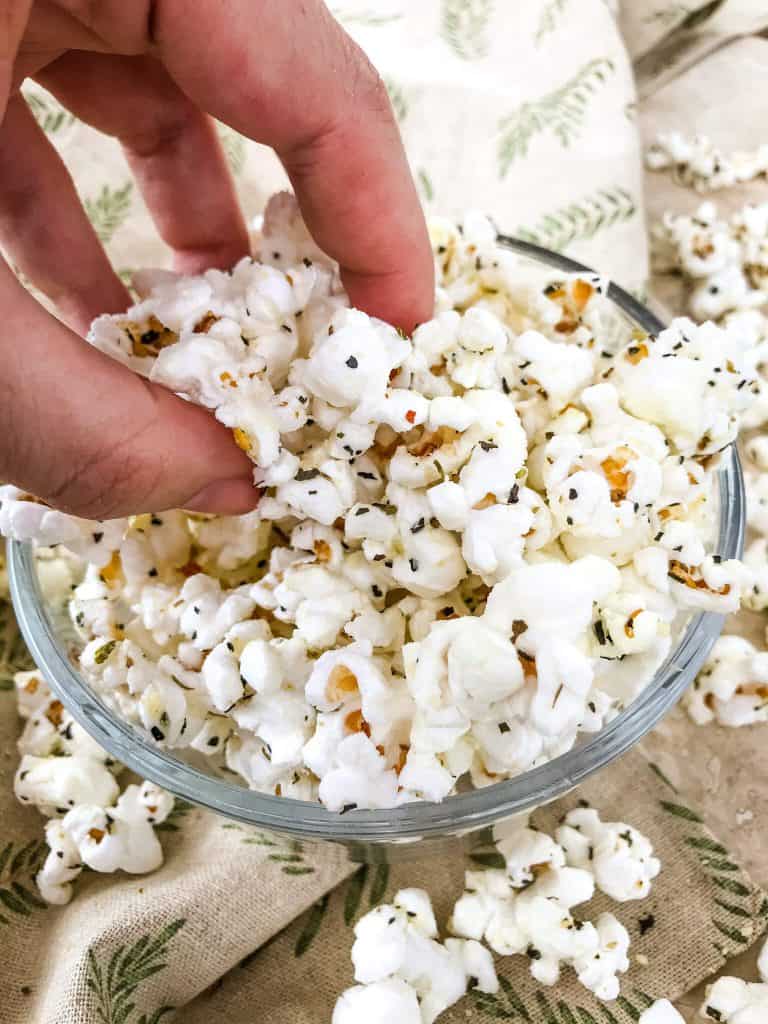 A hand grabbing popcorn out of a bowl