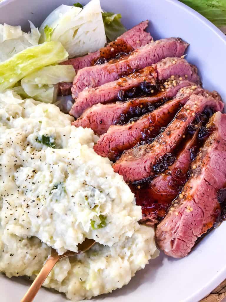 Sliced Guinness Corned Beef with colcannon and cabbage in a dish with a copper spoon