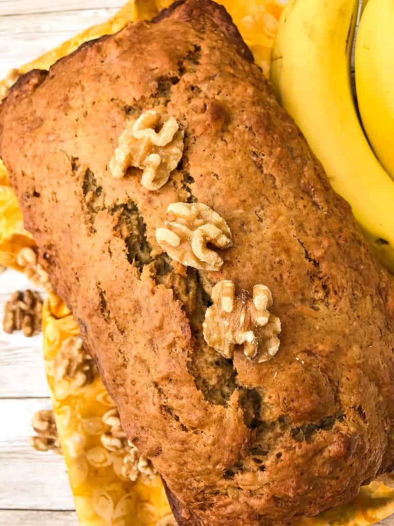 Full loaf of easy banana bread topped with walnuts next to bananas