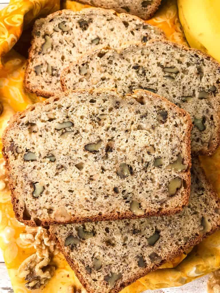 Close up of a slice of banana bread filled with walnuts on a yellow cloth