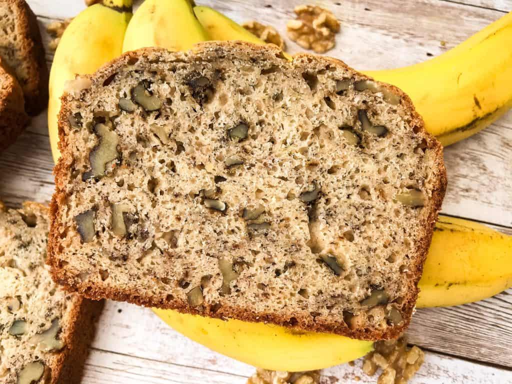 Close up of a slice of banana nut bread on top of bananas