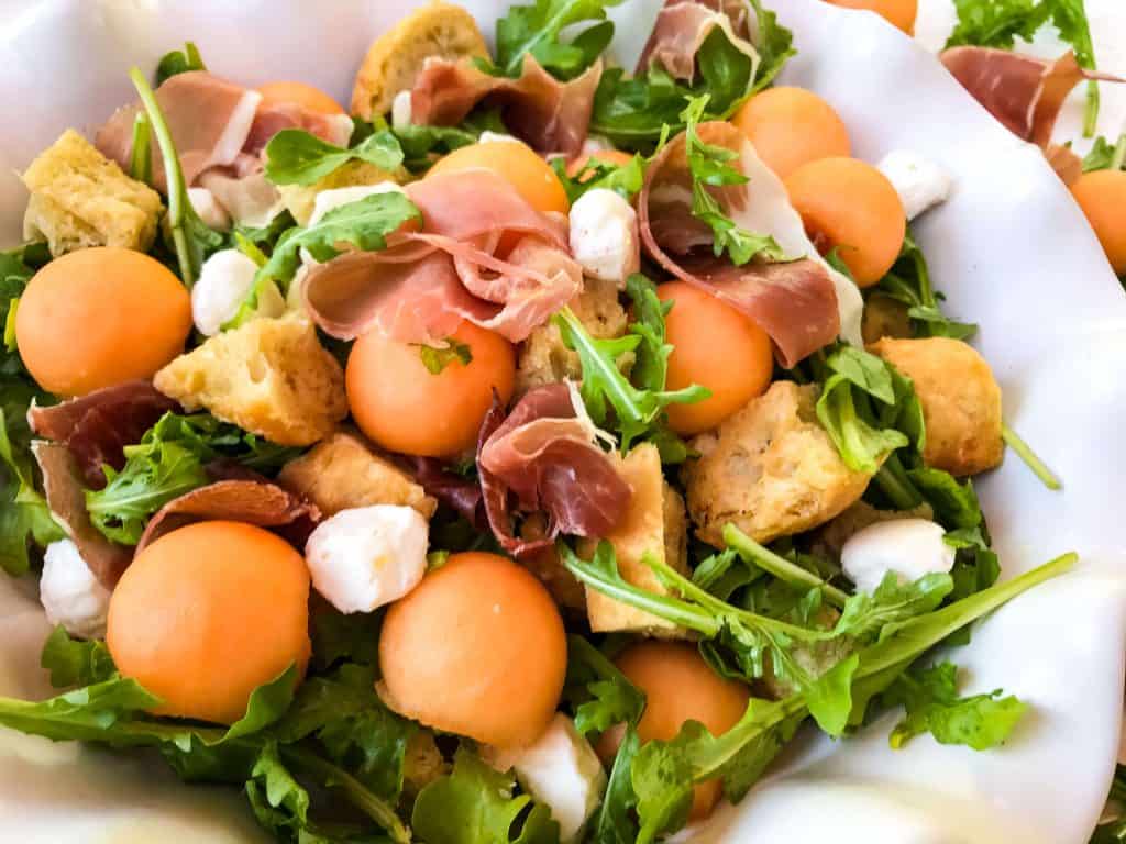 Horizontal image of Prosciutto Melon Panzanella Salad in a white bowl