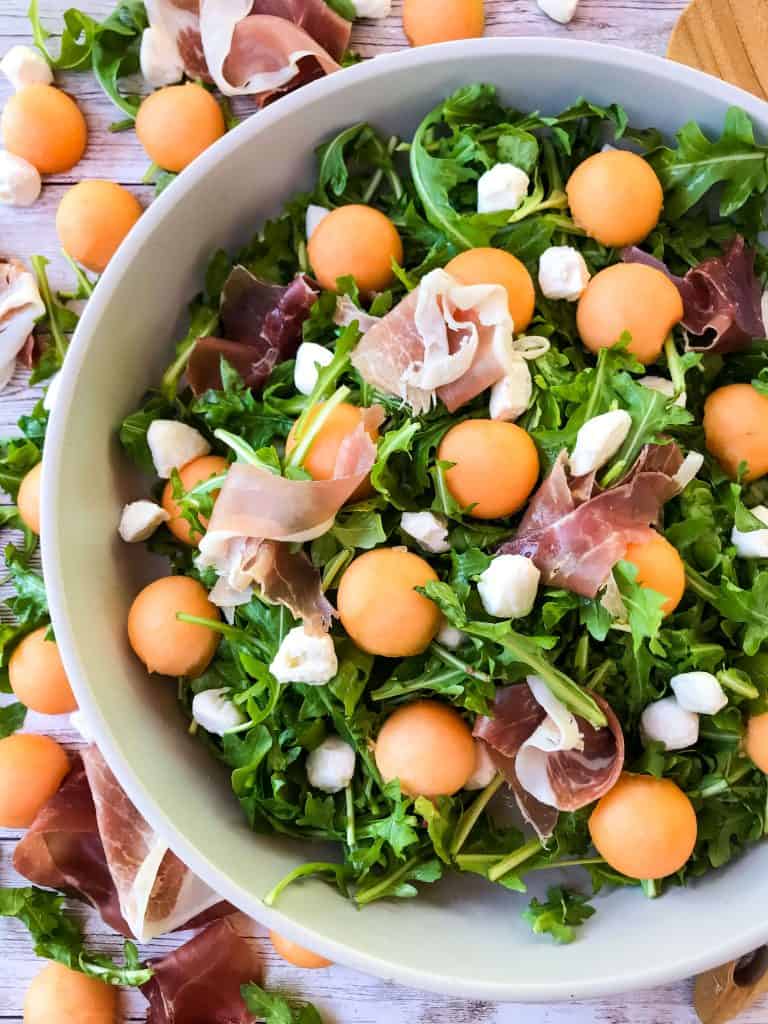 A bowl of salad with ingredients on the table next to it