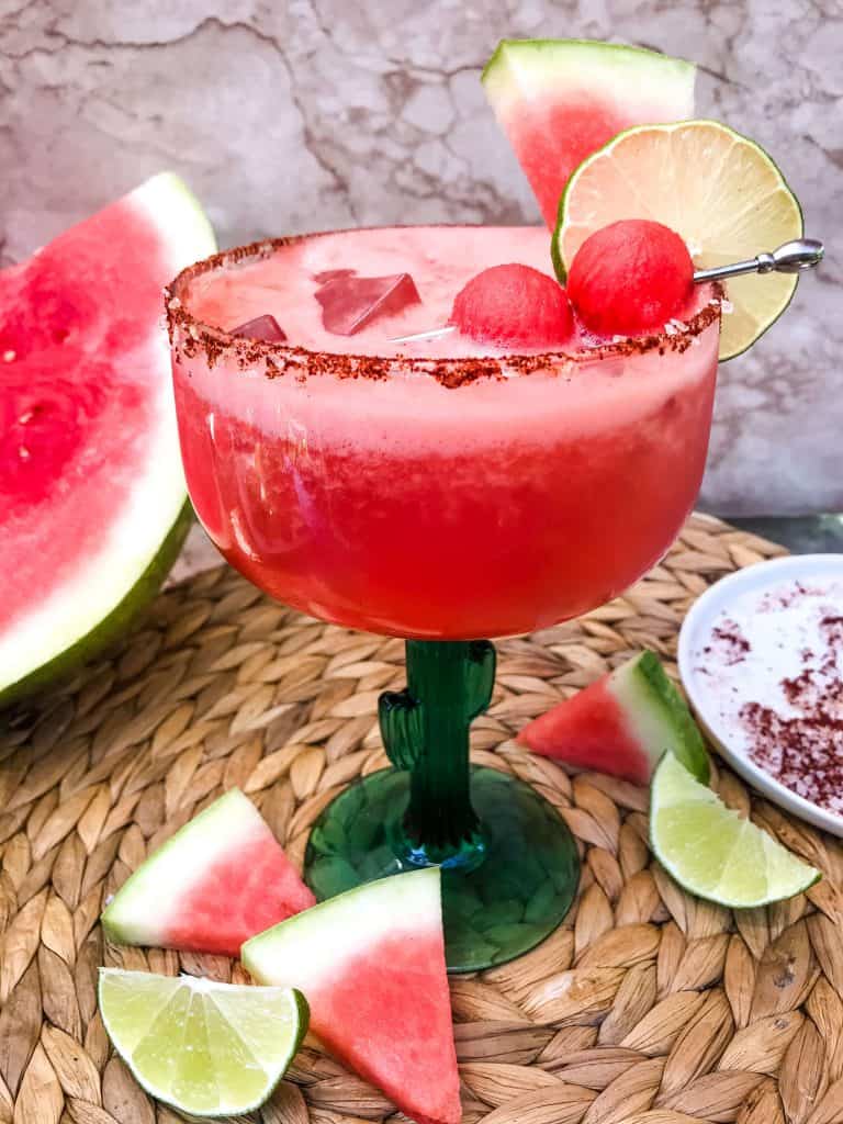 A Chile Lime Spicy Watermelon Margarita with watermelon and lime pieces around it