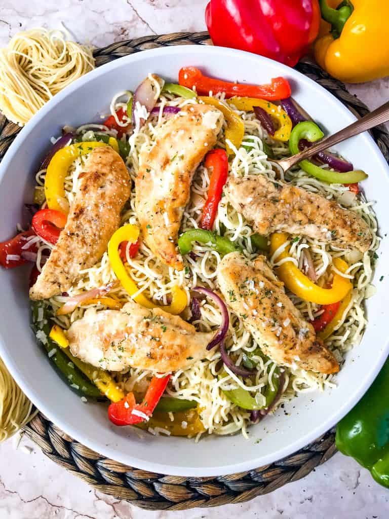A bowl of Copycat Olive Garden Chicken Scampi with a copper spoon surrounded by peppers and fresh pasta