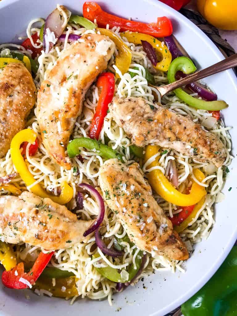 A bowl of Copycat Olive Garden Chicken Scampi with chicken tenders, red, yellow, and green bell peppers, and onion mixed with angel hair pasta