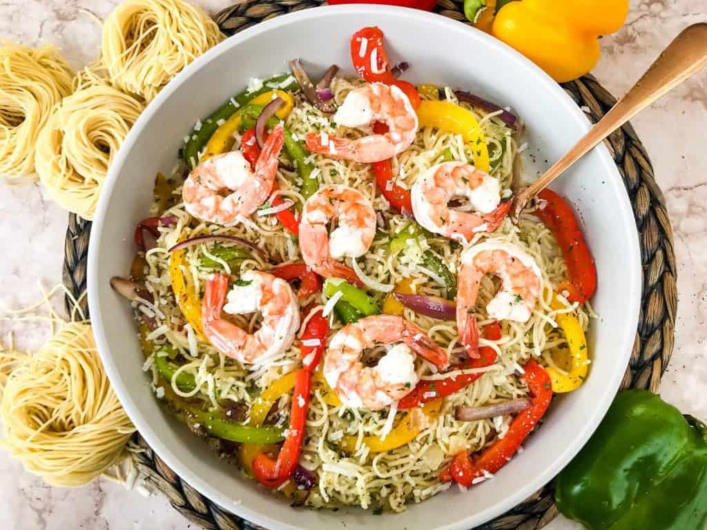 Horizontal bowl of Copycat Olive Garden Shrimp Scampi surrounded by fresh pasta and peppers with a copper spoon in it