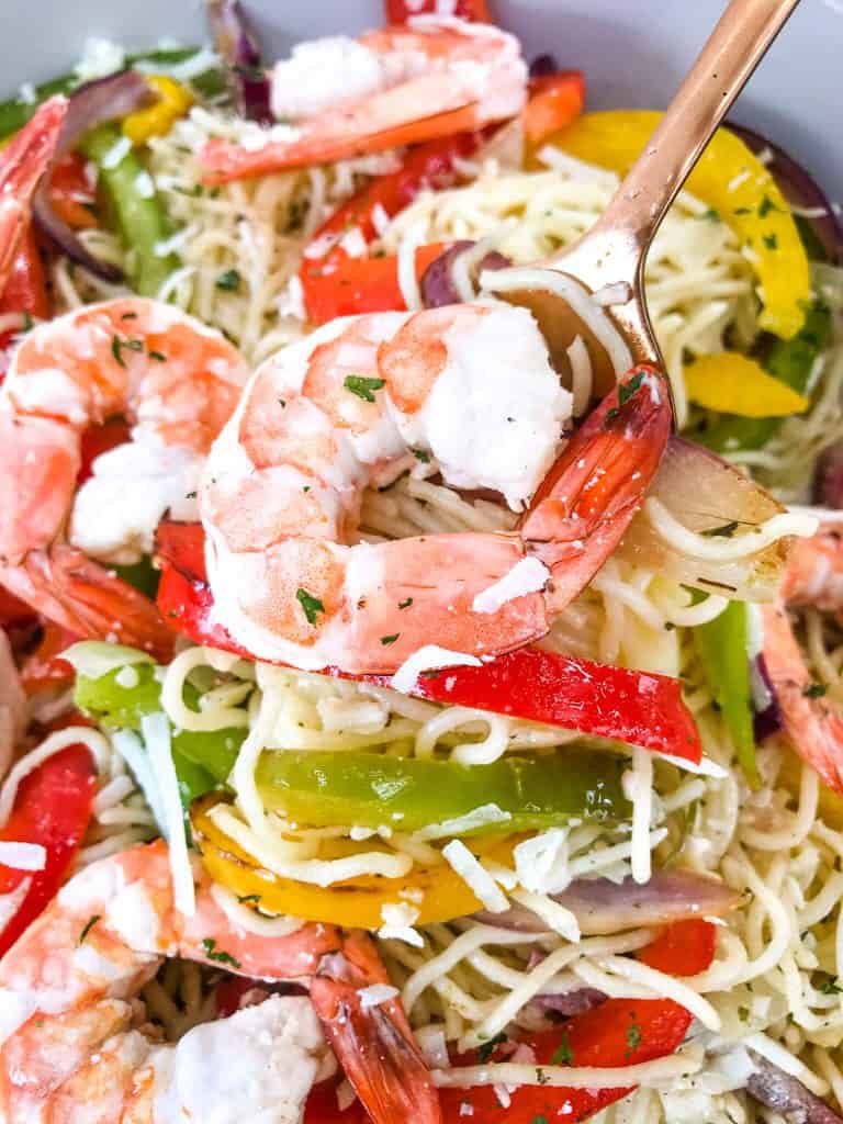 A copper spoon lifting a shrimp and some pasta out of the dish