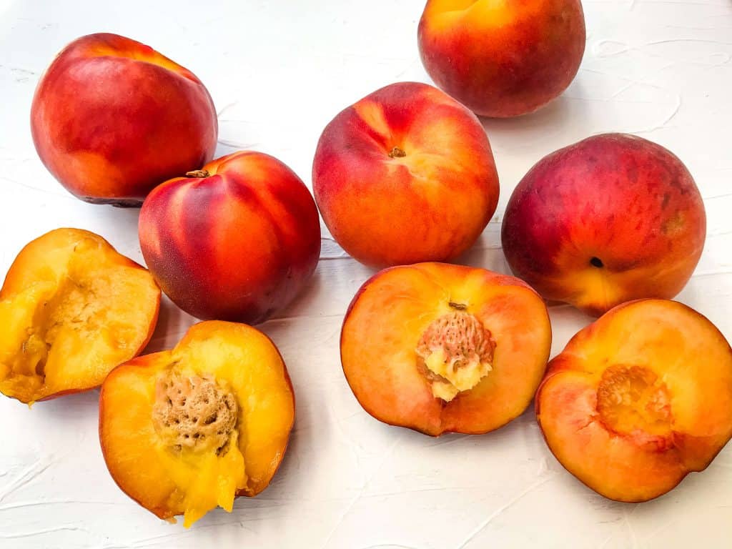 The Difference Between Peach and Nectarine side by side with cut and whole fruit on a white background