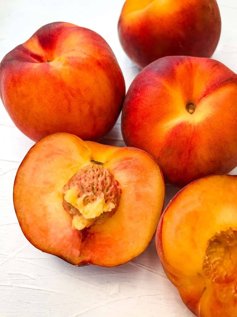 Close up of cut open peach and some whole peaches for the Difference Between Peach and Nectarine
