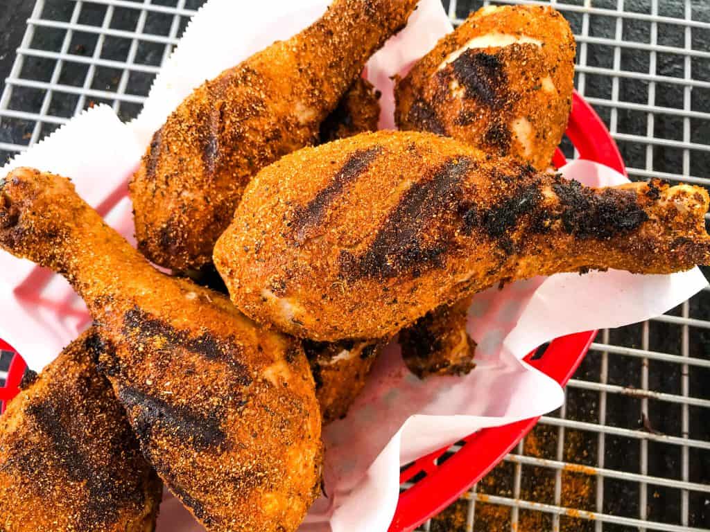 A basket of grilled chicken drumsticks coated in a dry rub in a basket
