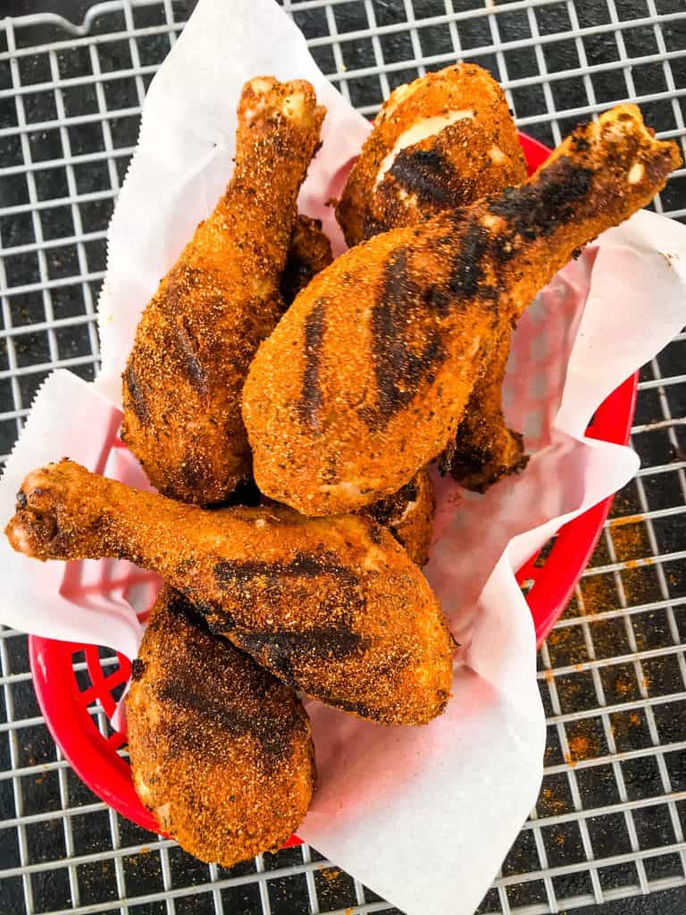 A red basket with white paper full of Dry Rub Cajun Grilled Chicken Drumsticks on a wire rack