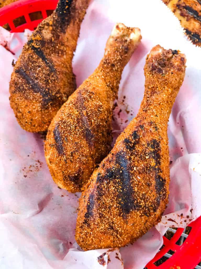 Three Dry Rub Cajun Grilled Chicken Drumsticks lined up in a red basket with white paper