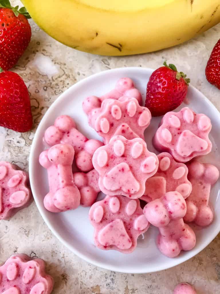 A plate of pink Frozen Strawberry Banana Dog Treats surrounded by fruit