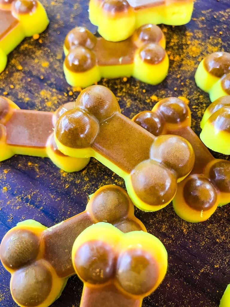 Stacked yellow and brown Frozen Turmeric Coconut Dog Treats on a black background