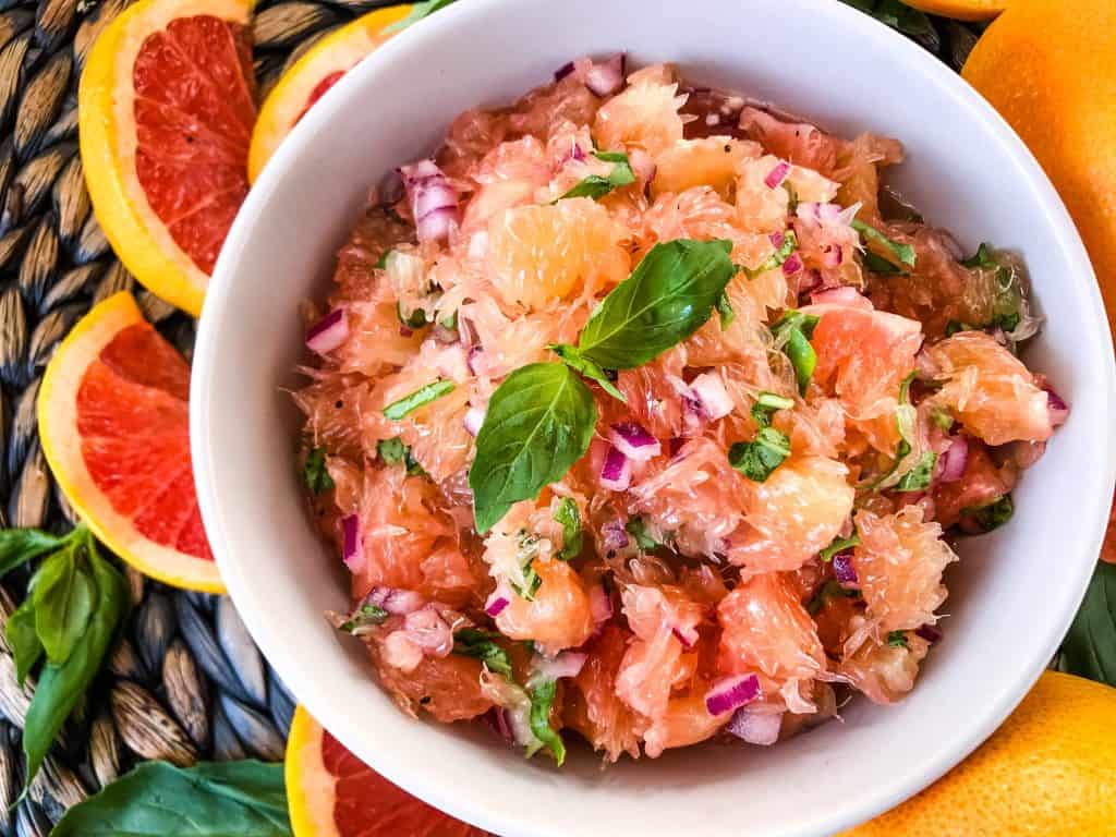 A grapefruit salsa in a bowl surrounded by fruit