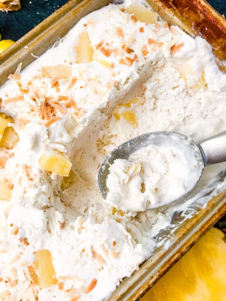 A pan full of No Churn Pina Colada Ice Cream with an ice cream scoop on top