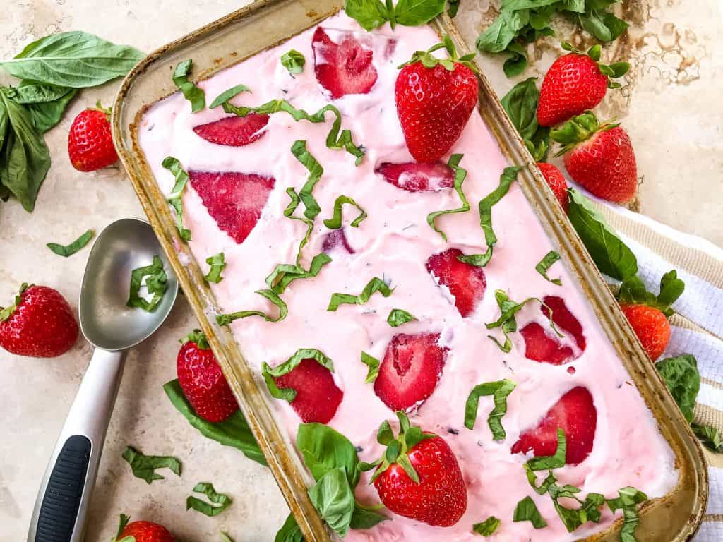 Bread loaf tin full of No Churn Strawberry Basil Ice Cream with strawberry slices and cut basil on top